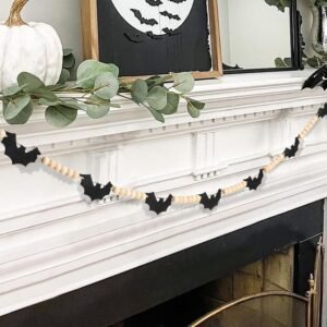 Black felt bat garland with natural wood beads draped across a white fireplace mantel decorated for Halloween