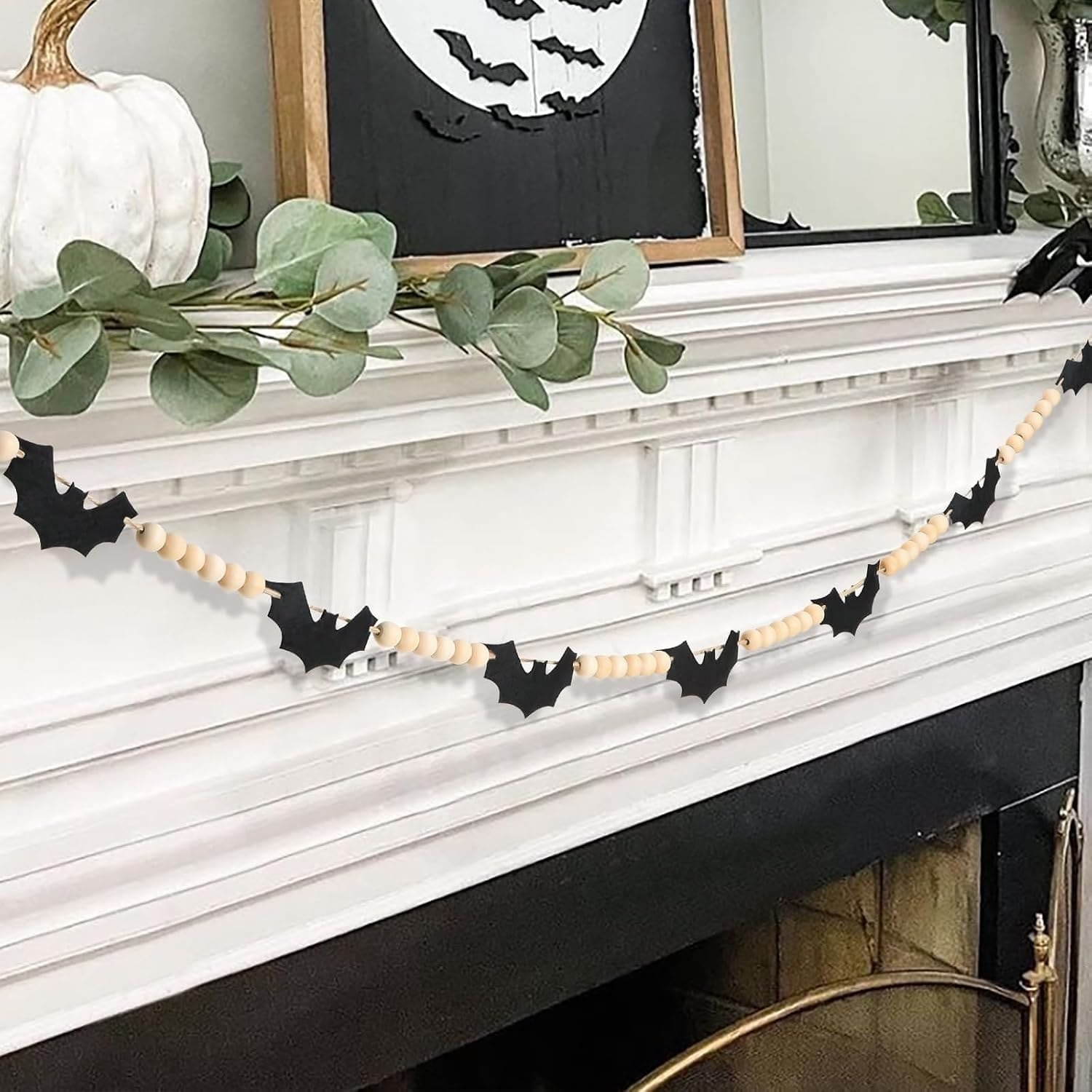 Black felt bat garland with natural wood beads draped across a white fireplace mantel decorated for Halloween