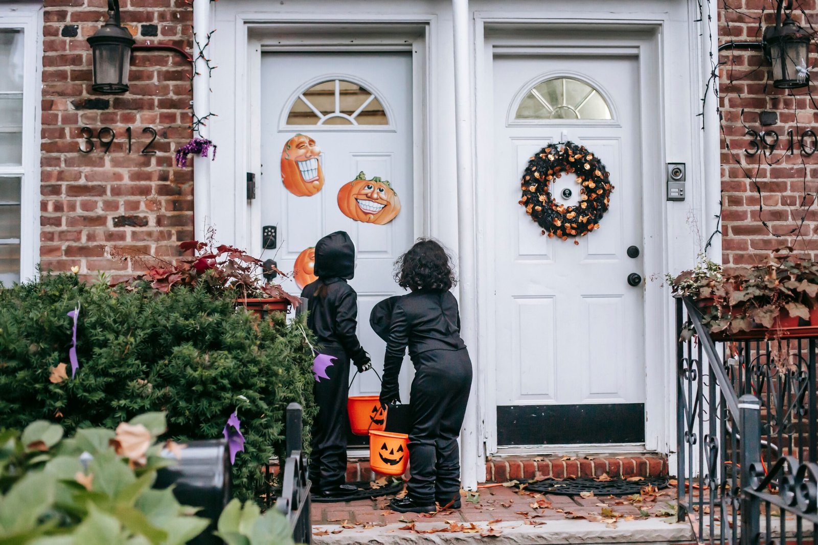 LED Halloween Wreath Safety: 5 Essential CPSC Rules for Front Door Displays 1 Two children in black Halloween costumes trick-or-treating with pumpkin candy buckets at a decorated front door