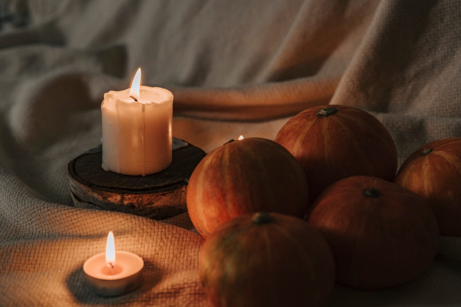 Fire-Safe Halloween Decorations: 5 Essential CPSC Rules for Flame-Free Display 1 Lit candles and small pumpkins arranged on burlap fabric for a cozy autumn atmosphere