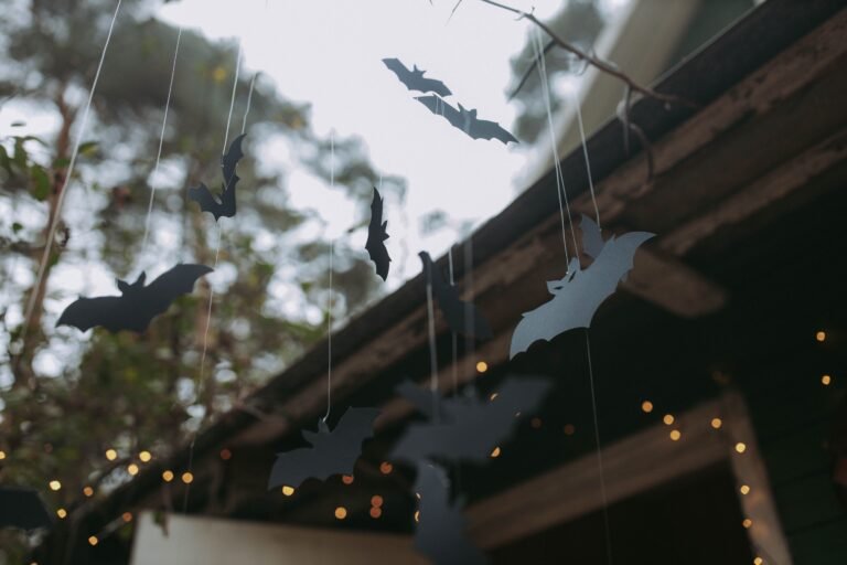 Hanging Halloween Ceiling Decorations: 5 Essential CPSC Rules for Safe Overhead Styling 1 Black paper bat cutouts hanging from strings under a wooden patio roof strung with string lights for Halloween